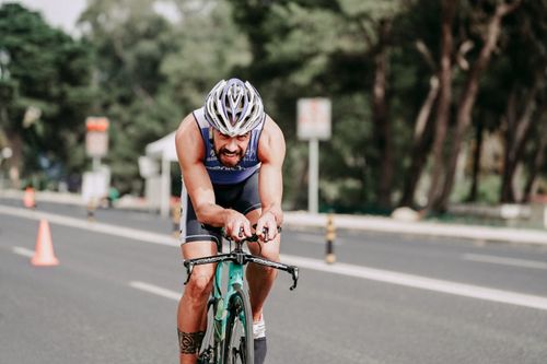 Free Muscular bearded man in protective helmet and sportswear cycling on empty asphalt road during competition and looking at camera Stock Photo