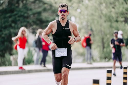 Strong muscular sportsman in sportswear and protective glasses running on asphalt road during competition