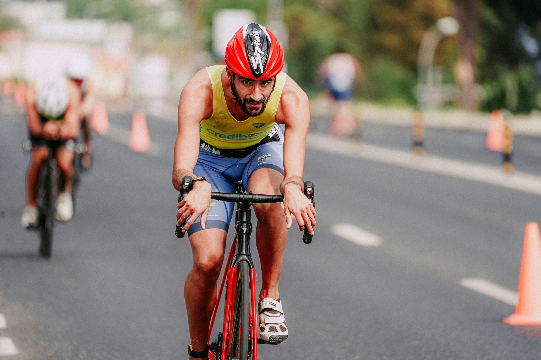Concentrated bearded man in protective helmet and sportswear cycling on asphalt road and looking at camera