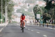Full body of strong man in helmet and sportswear cycling on empty asphalt street during competition