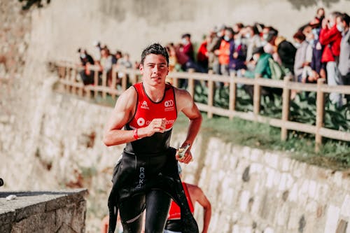 Muscular man in wet sportswear running fast during race and looking at camera