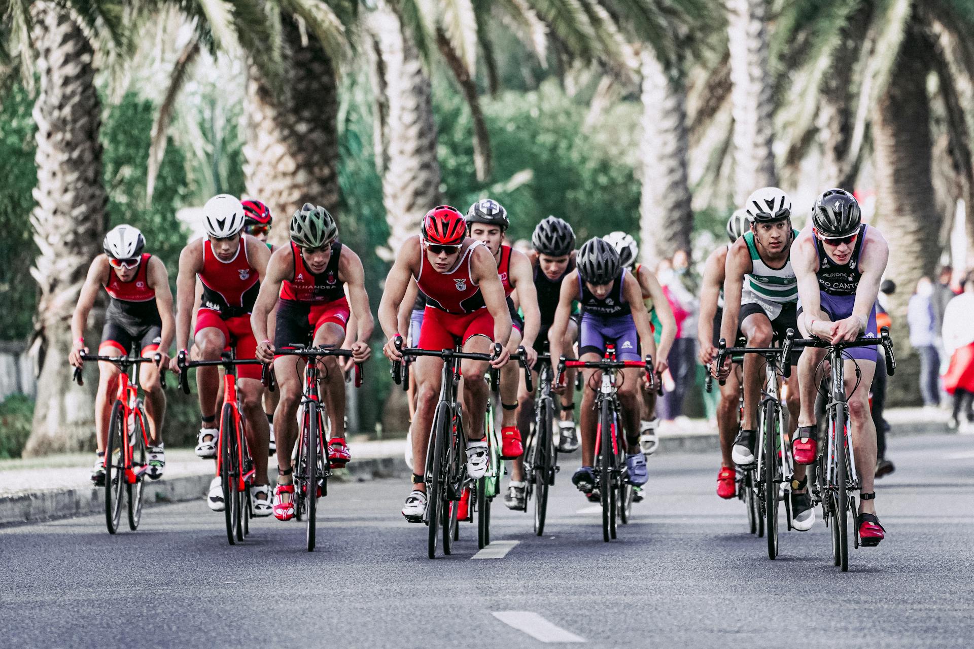 Group of people in protective helmets and sportswear riding bikes on asphalt road during competition