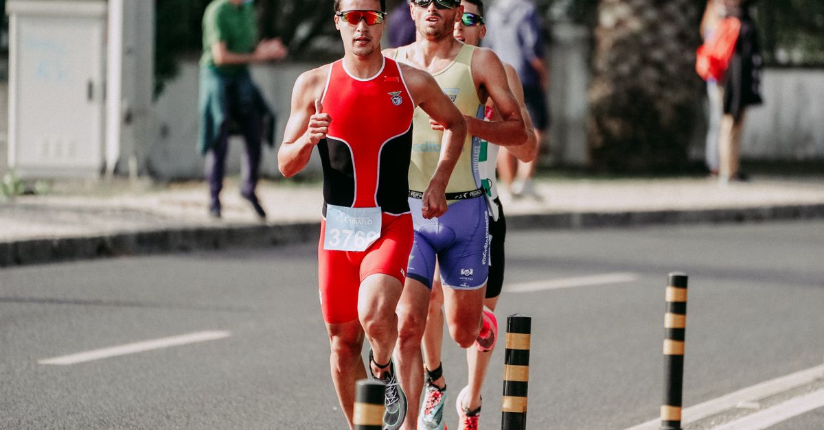 Runners in sunglasses striding down a sunlit asphalt road with arms raised in celebration after a Saturday social run.