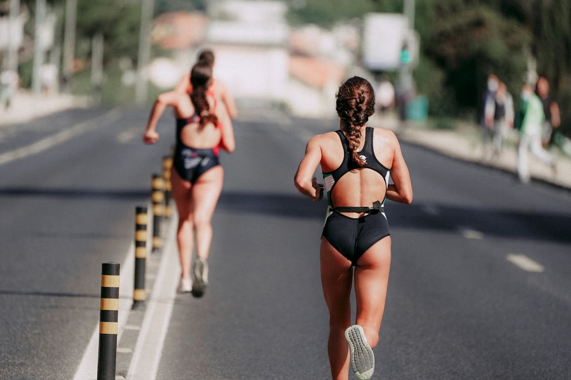 Faceless sportswomen running on asphalt road in daytime