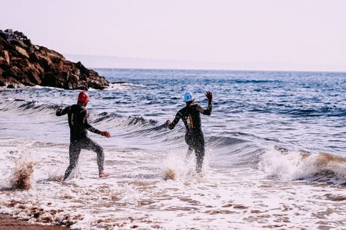 Free Full body side view of people in wetsuits and swim caps coming into wavy ocean in daytime Stock Photo