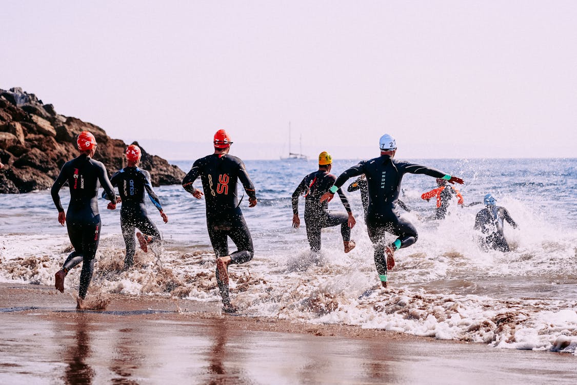 Free Faceless sportspeople in wetsuits entering sea Stock Photo