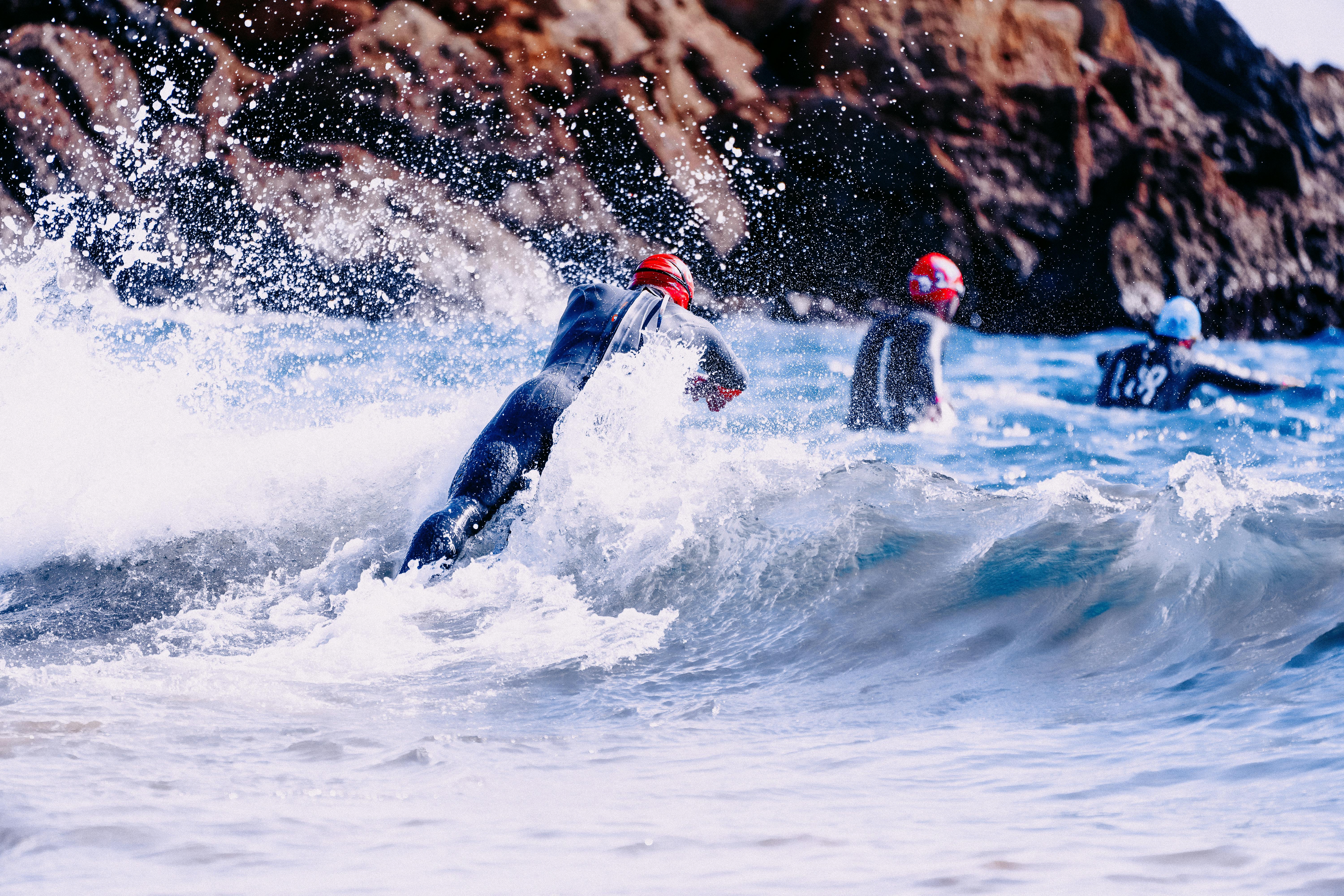 swimmers coming into wavy ocean next to cliff