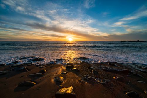 Free Capturing the golden sunset casting reflections over a rocky seashore with vibrant skies. Stock Photo