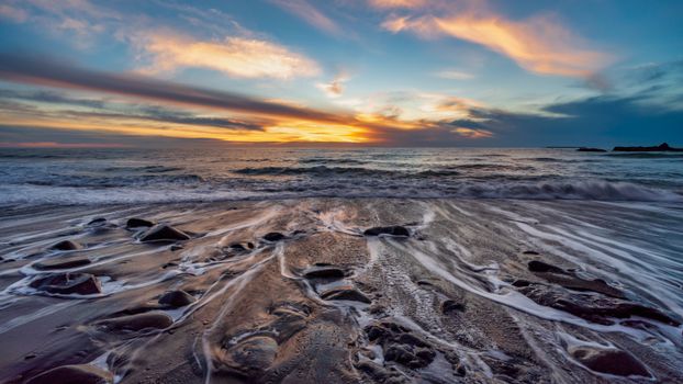 Captivating sunset over a tranquil beach with colorful skies and gentle waves flowing over smooth stones.