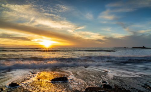 Free Captivating sunset at the beach with vibrant clouds and dynamic waves crashing on the shore. Stock Photo