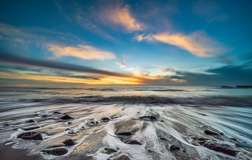 Free Stunning sunset over the ocean with rocky shore and colorful sky. Stock Photo