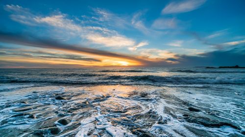 Free Dramatic ocean sunset with waves crashing against a rocky shore, under a moody, colorful sky. Stock Photo