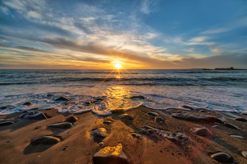 Free Stunning sunset view over a rocky beach with sun reflections on the ocean waves. Stock Photo