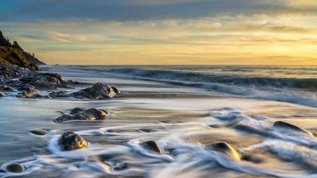 Peaceful seashore scene with smooth waves and rocks during sunset, ideal for nature wallpapers.