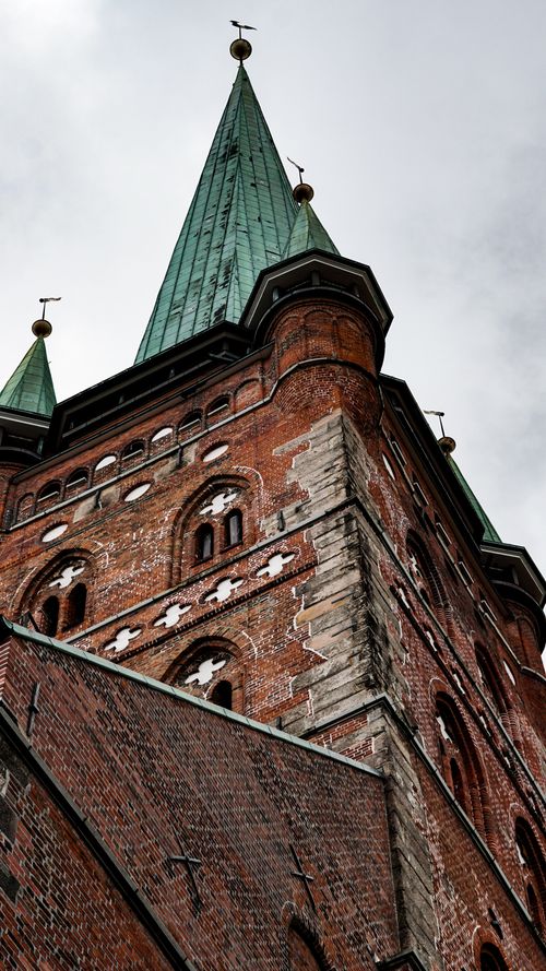 Free A dramatic view of a Gothic church tower with green spires under an overcast sky. Stock Photo