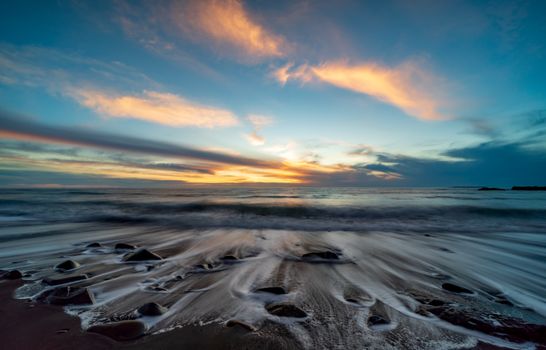 Serene beach sunset with dramatic clouds and gentle waves on a summer evening.