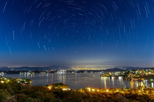 Long exposure of star trails over a city and lake, showcasing a vibrant night sky.