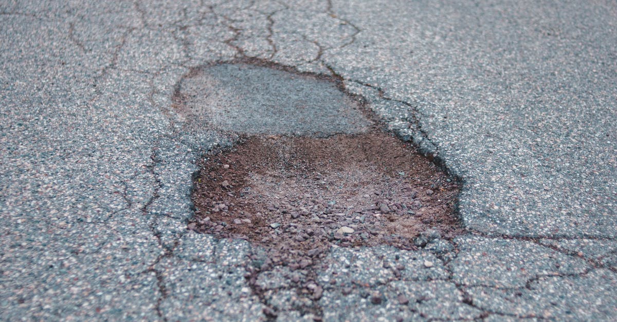 Photo by Erik Mclean Empty rural road with a large pothole, leading through a tranquil and desolate wooded area.