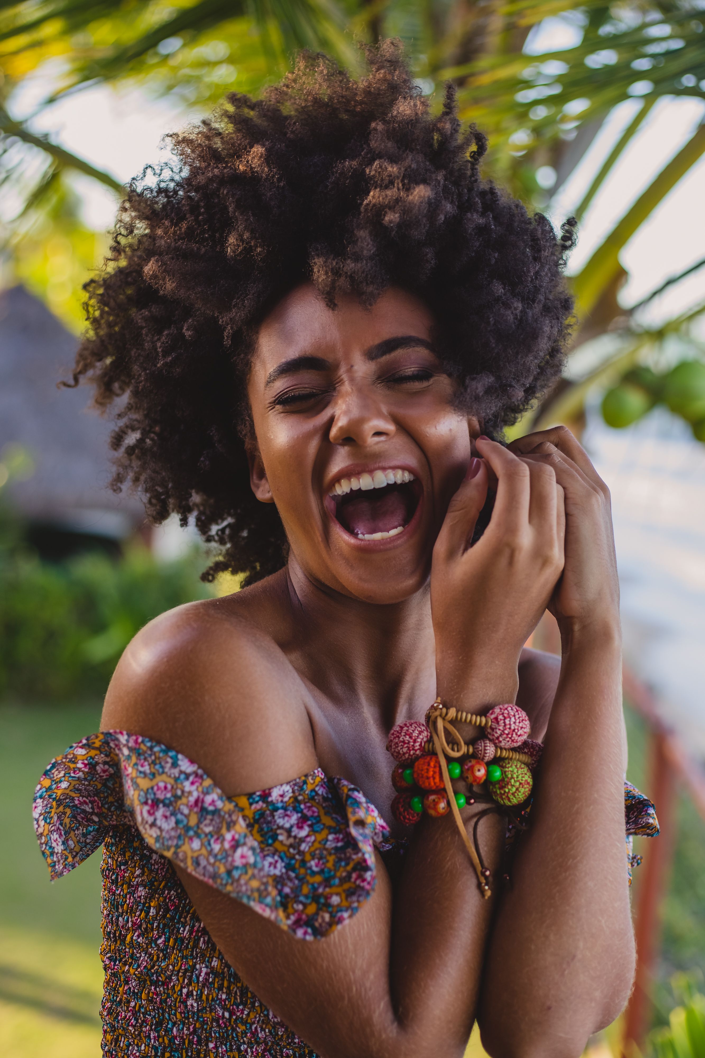 一位快乐的黑人女游客身着时髦服装，留着非洲发型，正闭着眼睛触摸自己的脸庞