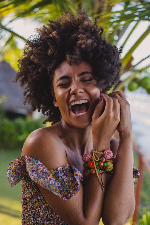 Happy black female tourist in trendy wear with Afro hairstyle touching face with closed eyes