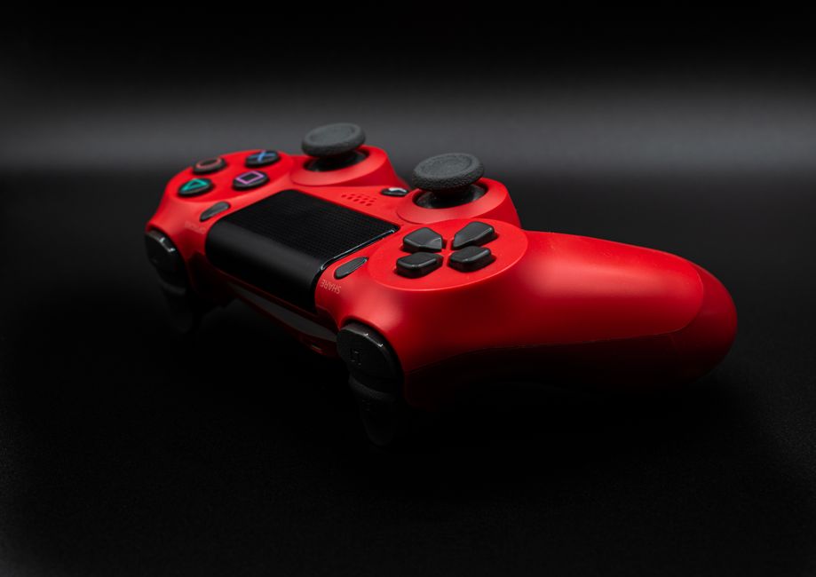 Close-up of a red gaming controller on a dark surface, highlighting its buttons and design.