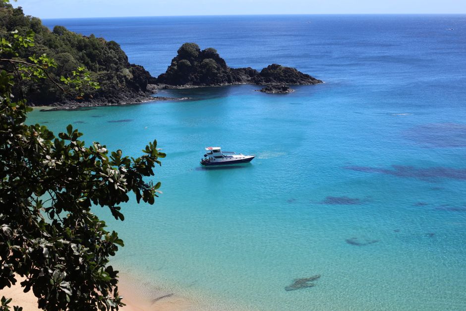 A breathtaking aerial view of a clear turquoise bay in Brazil with a boat and lush cliffs.
