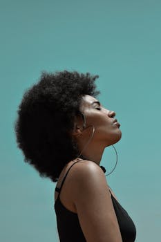 从侧面看去，一位年轻的反思种族女模特戴着大耳环，在蓝天下闭着眼睛