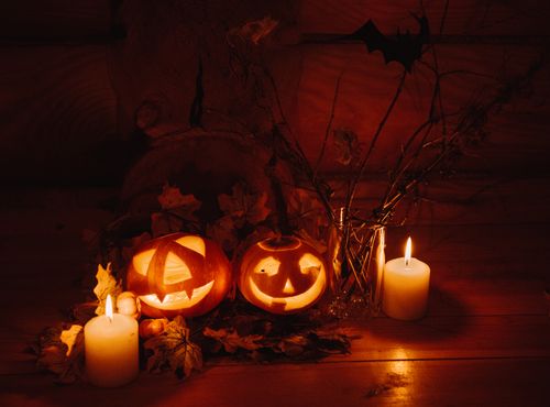 Free Cozy Halloween scene featuring glowing jack-o'-lanterns and candles among autumn leaves. Stock Photo