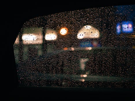 Moody night scene through car window with raindrops and city lights in Montreal.