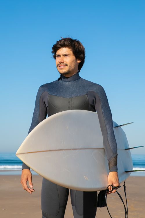 Free Man in wetsuit holding a surfboard on a sunny beach in Portugal, ready for surfing. Stock Photo