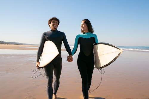 2 Femmes En Combinaison Humide Bleue Et Noire Tenant Une Planche De Surf Blanche Sur La Plage