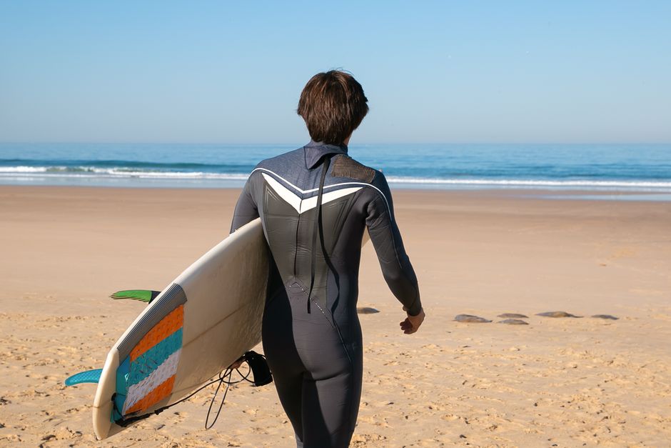 Man walking on a sunny Portuguese beach, carrying a surfboard and wearing a wetsuit.