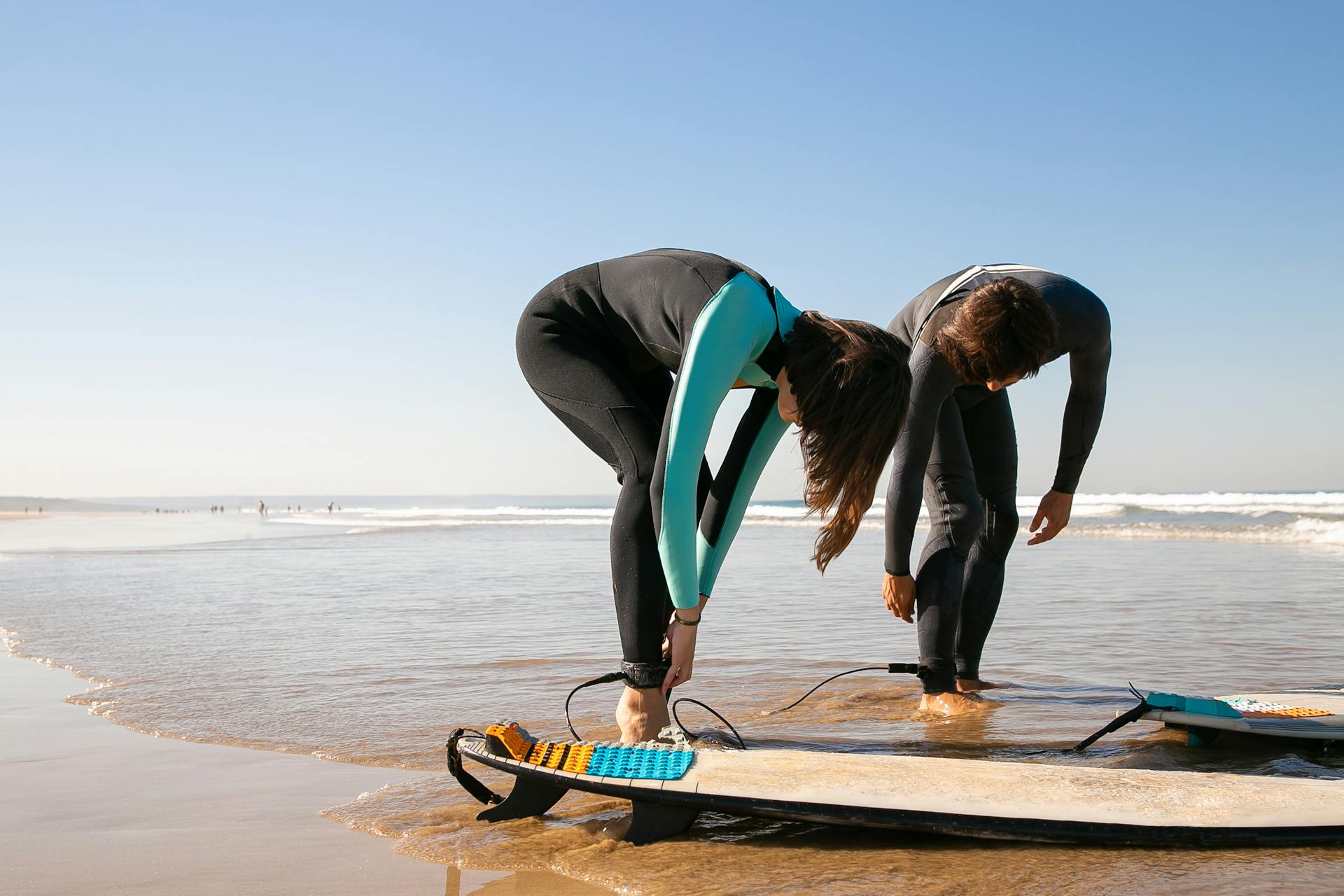 Photo of a Man and a Woman Putting on Their Surfboard Leashes