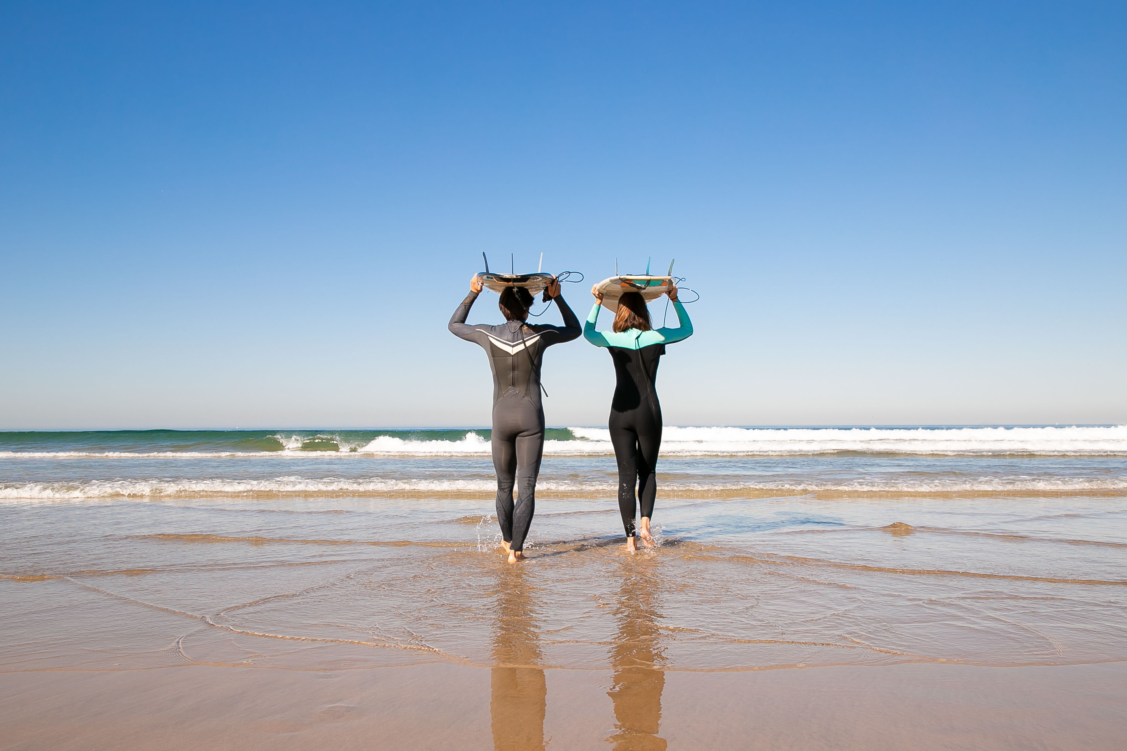 A couple walking on a Portuguese beach with surfboards, enjoying a sunny day and ocean views.