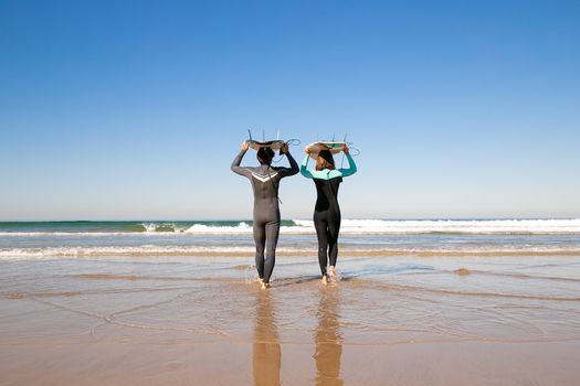 A couple walking on a Portuguese beach with surfboards, enjoying a sunny day and ocean views.