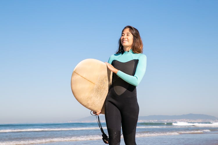 Woman In A Wetsuit Carrying Her Surfboard