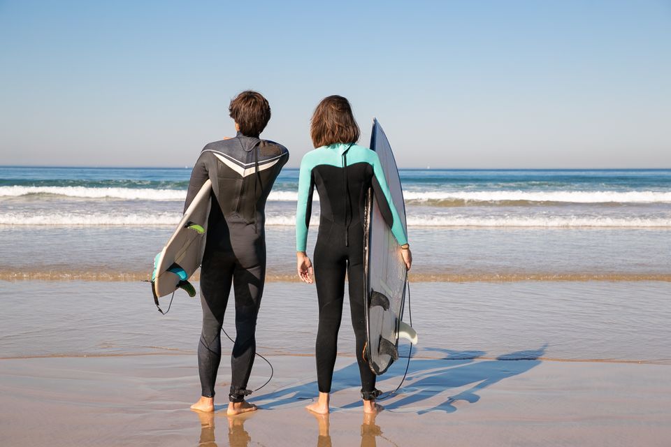 Back view of surfers holding boards on a sunny beach in Portugal.
