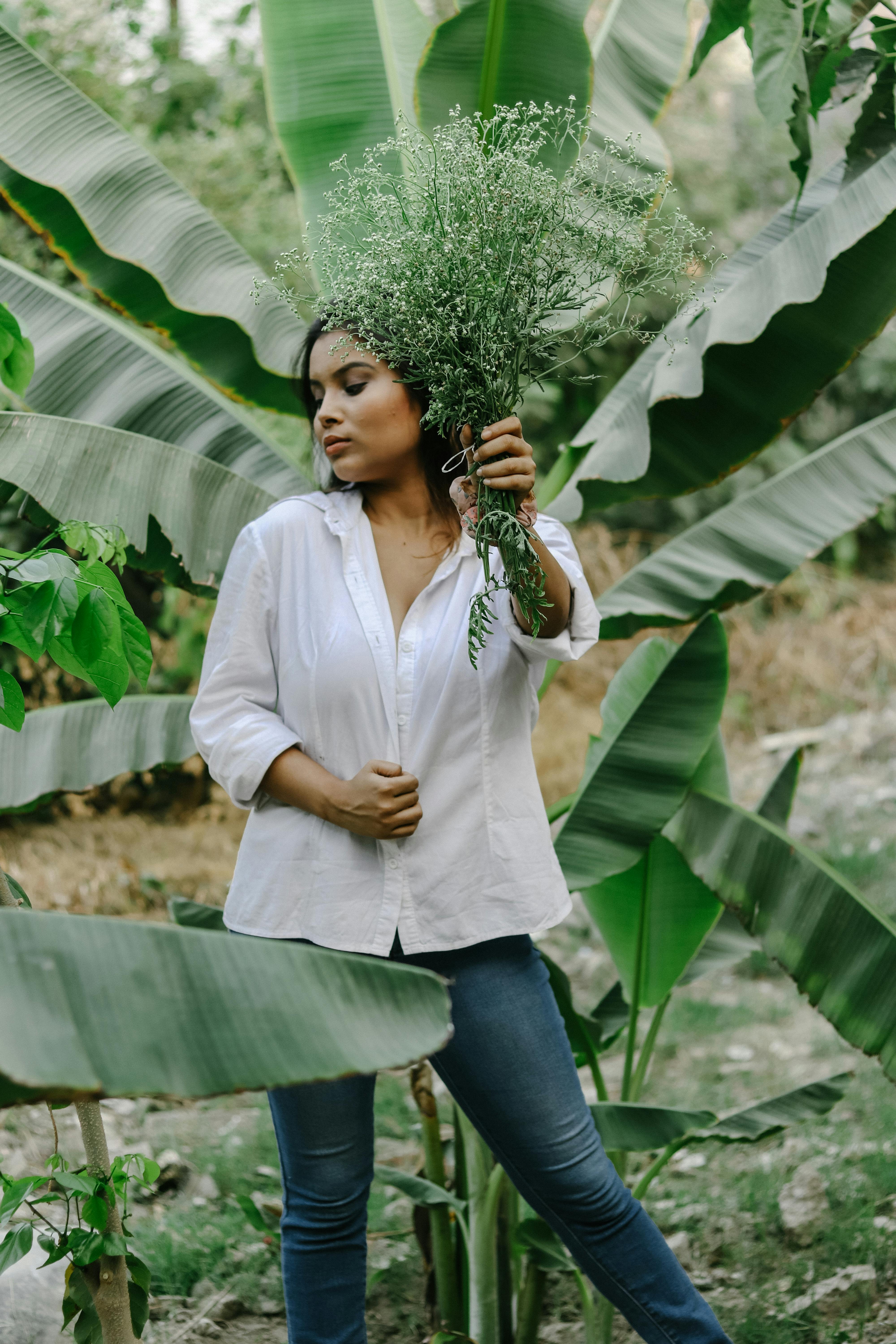 一位年轻女子手捧花束，在郁郁葱葱的热带植物间静立，时光宁静