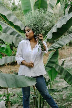 一位年轻女子手捧花束，在郁郁葱葱的热带植物间静立，时光宁静