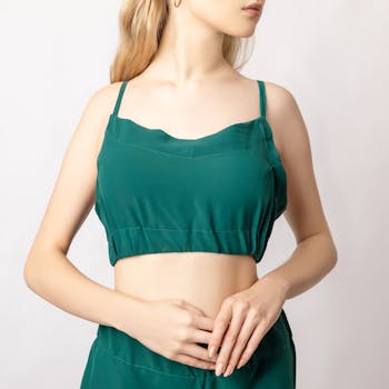 Crop faceless female in green top revealing bare belly standing against white background in studio