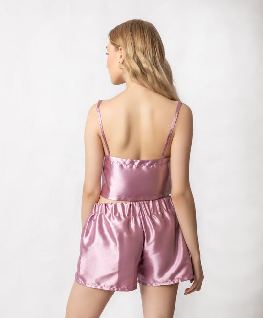 Back view of anonymous female wearing trendy pink silk sleepwear with bare back standing in studio