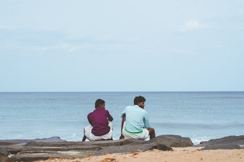 Men Sitting Together on Gray Rock Near Water