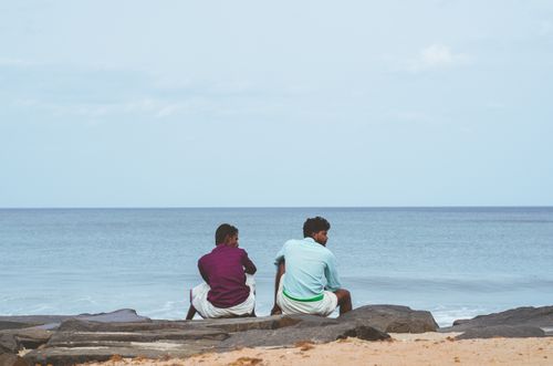 Free Two men sitting on rocks by the Puducherry coastline, enjoying a clear day by the sea. Stock Photo