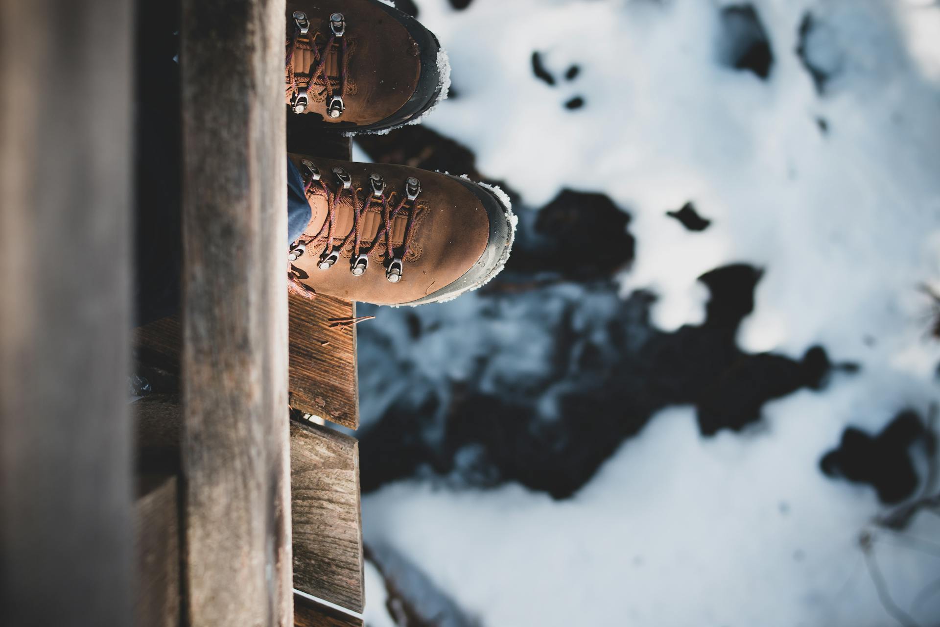 Top view of brown hiking boots on a wooden edge overlooking a snowy landscape, capturing a winter adventure.