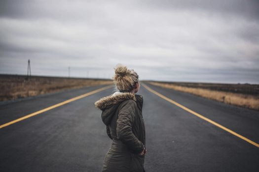 阴沉的天空下，一名穿着冬装的女子站在荒无人烟的路上，显得格外孤独
