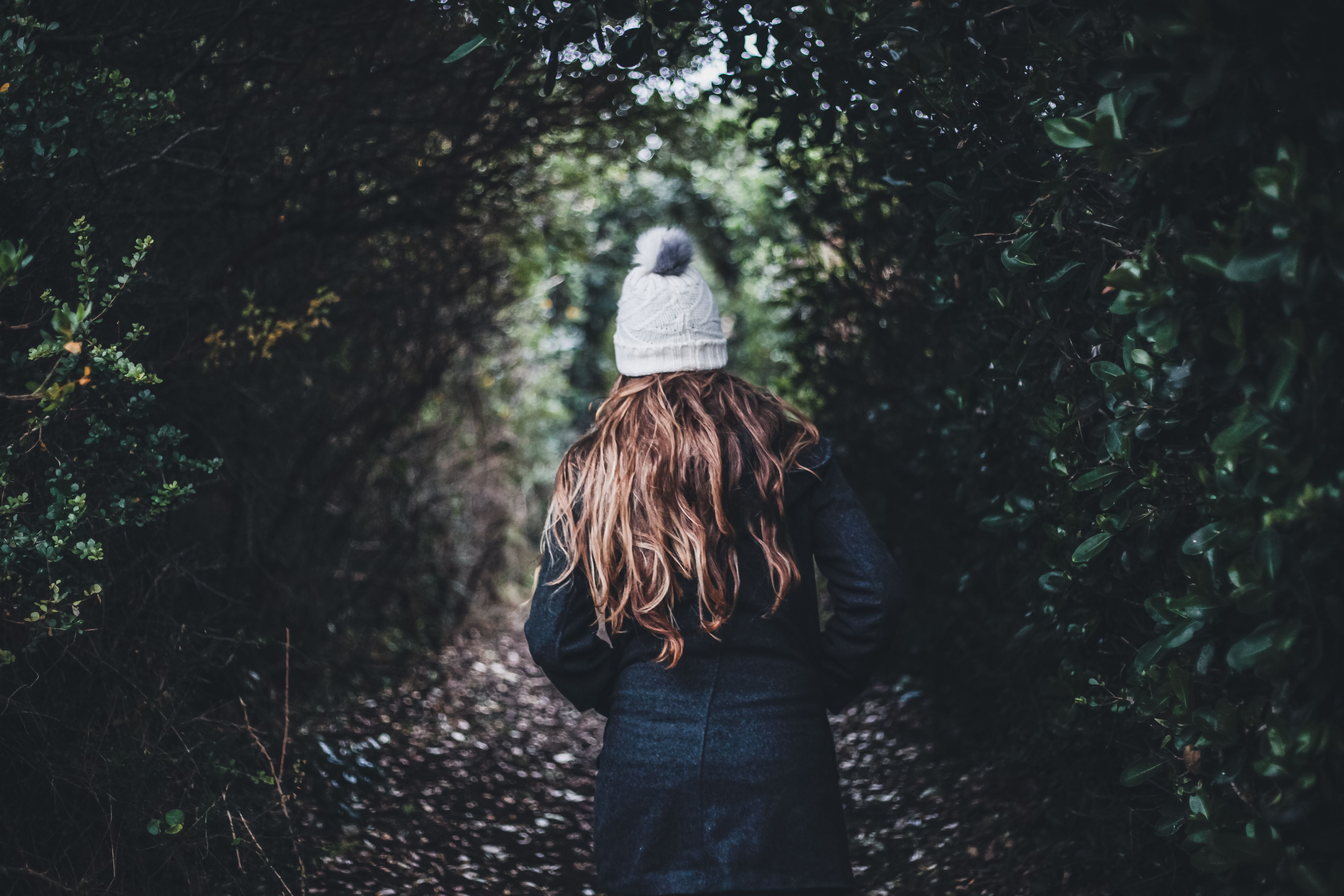 A woman walking a quiet forest path lined with tall trees, seen from behind