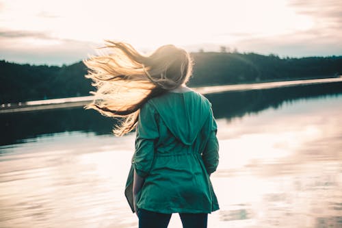 Free A Woman in Green Jacket Standing Near the Body of Water Stock Photo