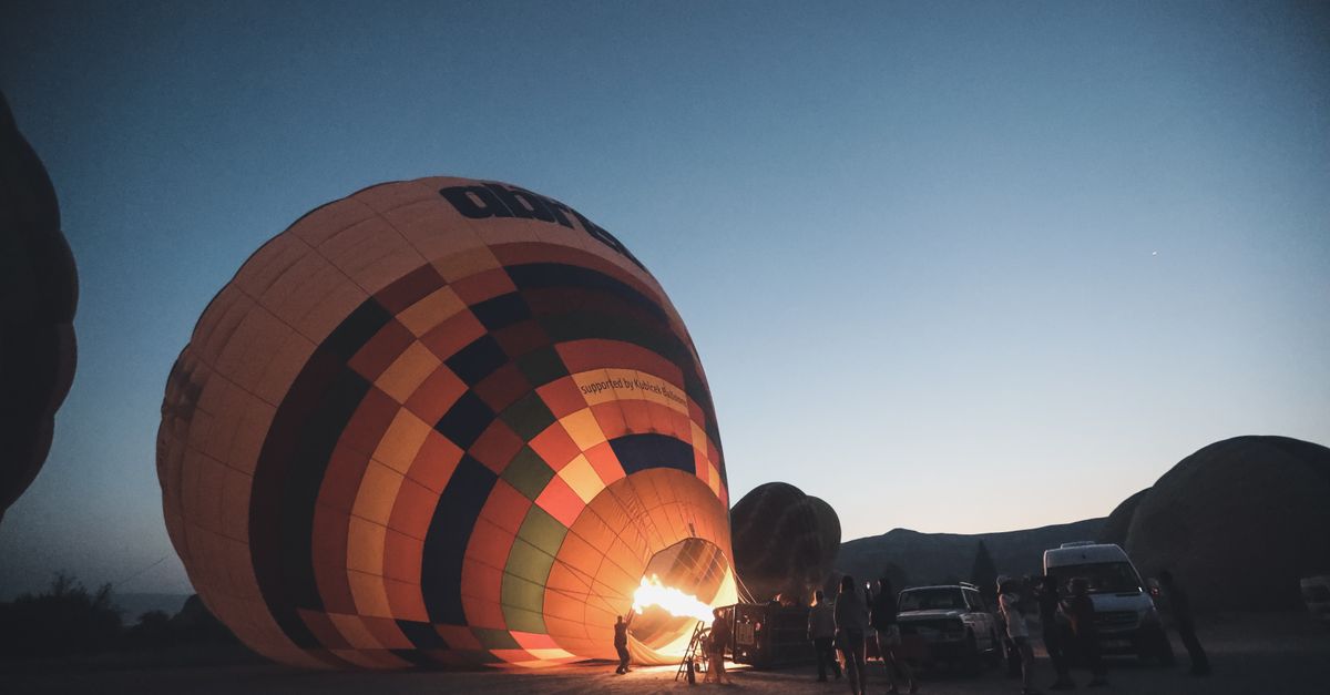 Vibrant hot air balloon inflating at dawn with silhouettes of people watching.