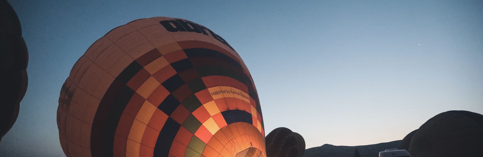 Vibrant hot air balloon inflating at dawn with silhouettes of people watching.