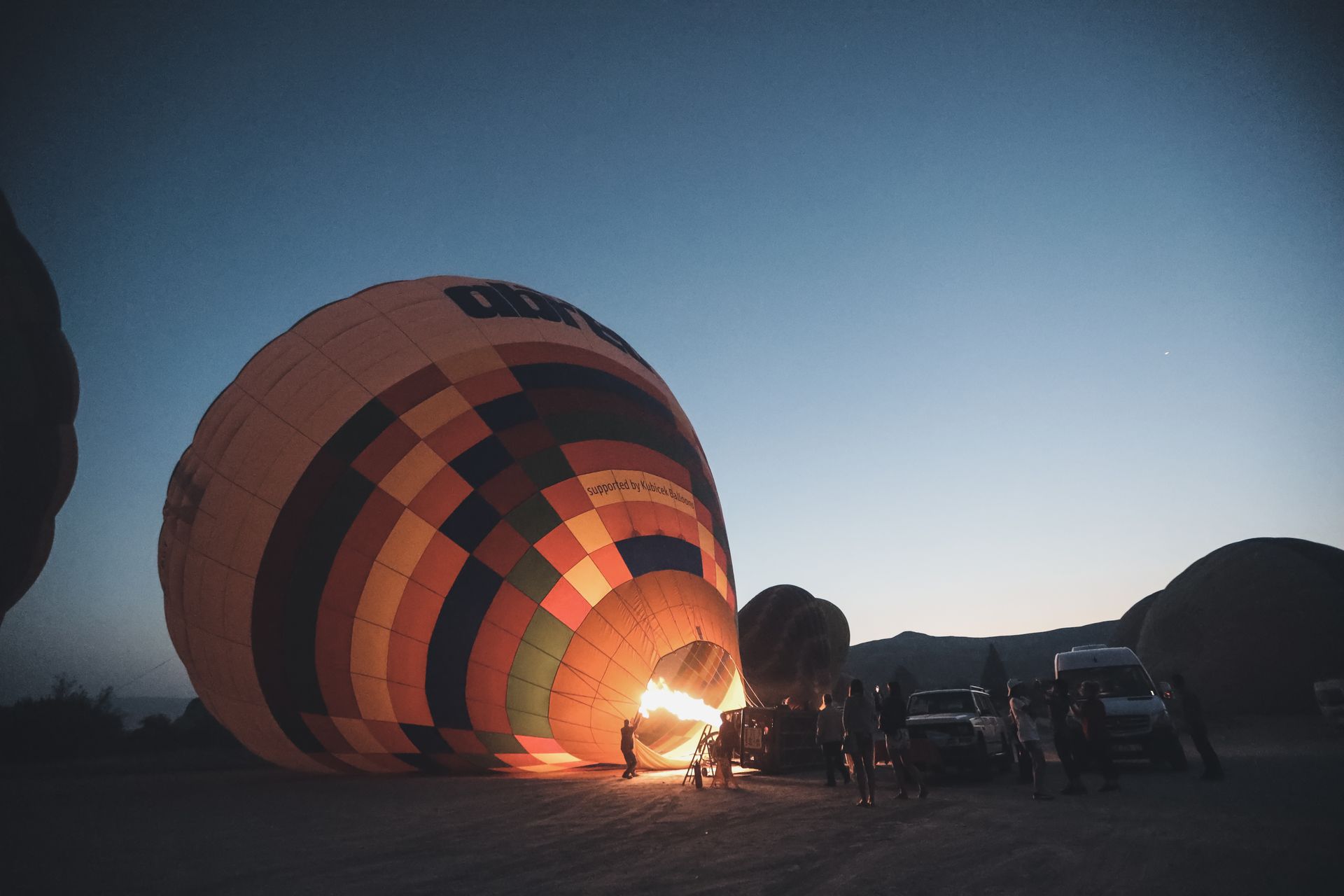 Vibrant hot air balloon inflating at dawn with silhouettes of people watching.
